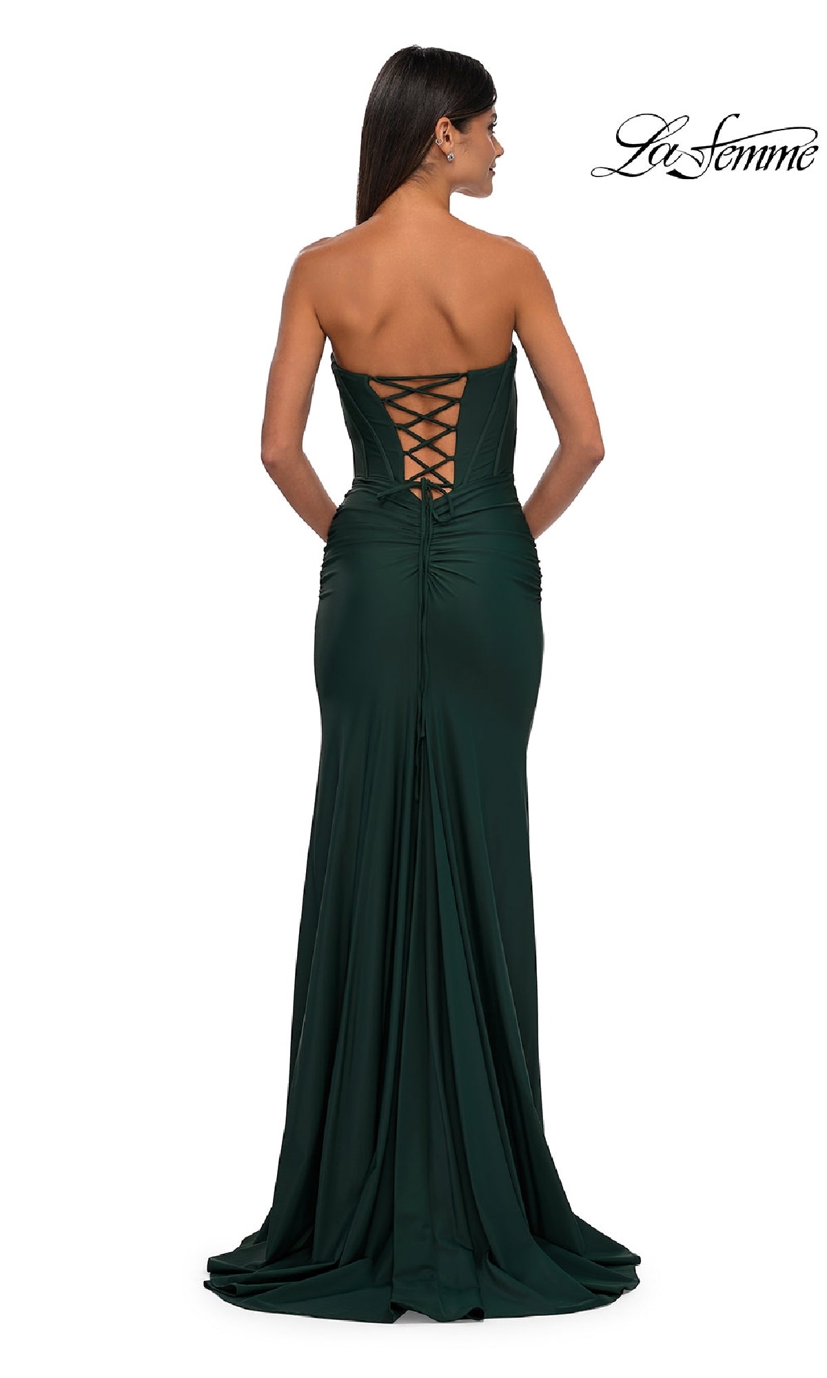 A woman faces away, wearing the Strapless Sweetheart Prom Gown: La Femme 32843 in dark green, showcasing its lace-up corset back and elegant floor-length silhouette.